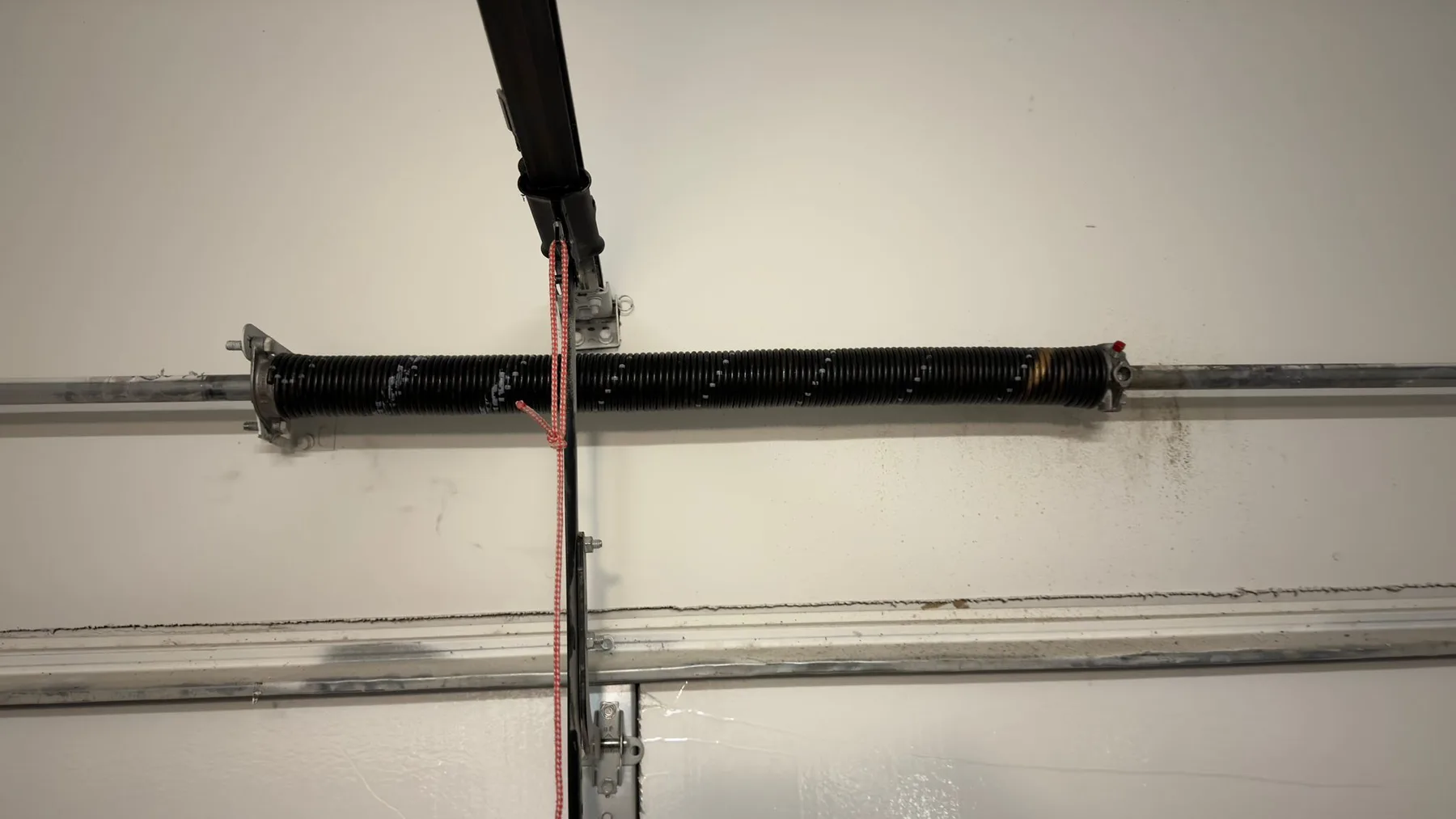 Black torsion spring and shaft mounted above a white garage door in Shockwave's Austin-area work gallery.